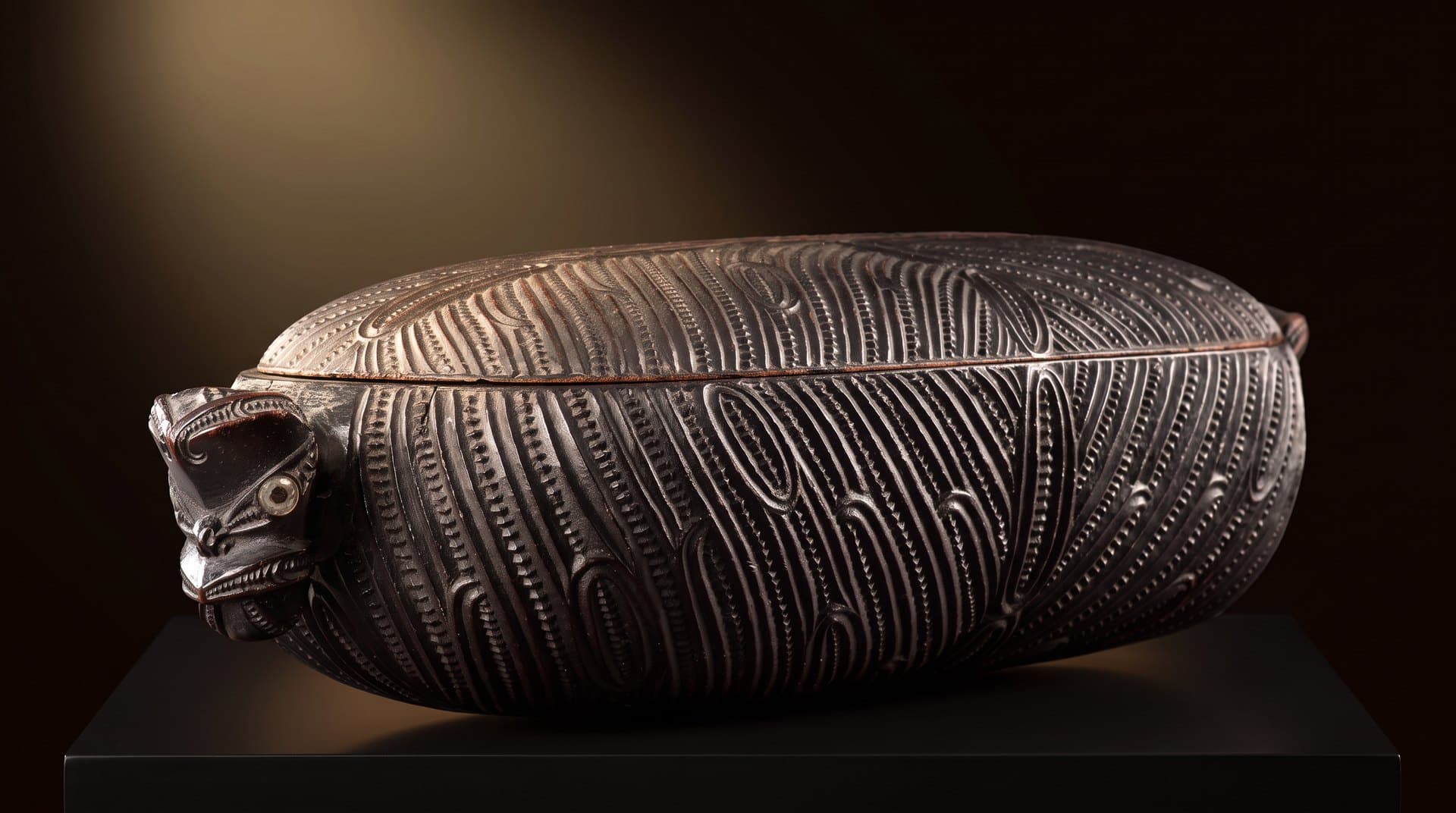 A carved wooden wakahuia, lit on a dark stage